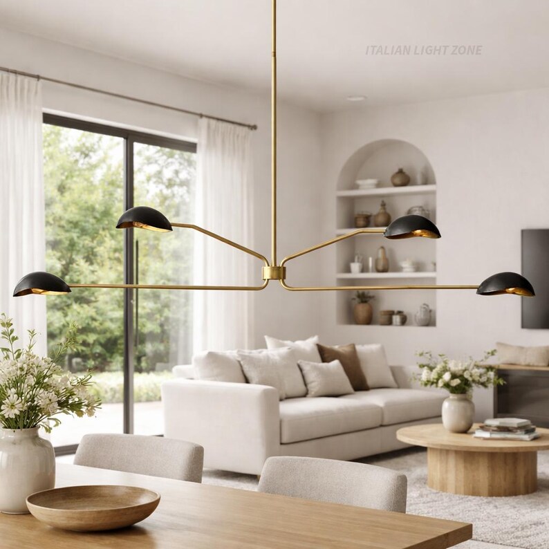 Pode incluir: Um lustre moderno, dourado, com quatro luzes pretas em forma de c&uacute;pula. A lumin&aacute;ria est&aacute; suspensa no teto e ilumina uma sala de estar com um sof&aacute; branco, uma mesa de madeira e janelas grandes. O texto "ITALIAN LIGHT ZONE" &eacute; vis&iacute;vel.
