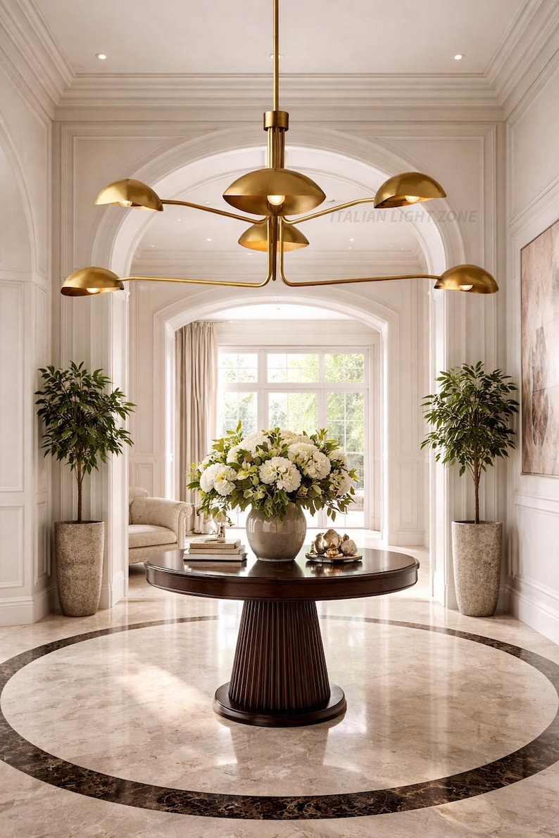 Pode incluir: Uma entrada elegante com um candelabro dourado, uma mesa redonda de madeira escura com um arranjo floral e plantas em vasos. O ch&atilde;o de m&aacute;rmore tem um padr&atilde;o circular. O texto "ITALIAN LIGHT ZONE" &eacute; vis&iacute;vel.