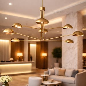 Pode incluir: Um lustre moderno dourado com v&aacute;rios bra&ccedil;os curvos, cada um com uma lumin&aacute;ria em forma de c&uacute;pula. A lumin&aacute;ria est&aacute; suspensa no teto em um espa&ccedil;o interior bem iluminado. O texto "ITALIAN LIGHT ZONE" &eacute; vis&iacute;vel.