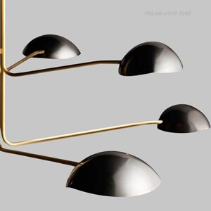 Pode incluir: Candeeiro de teto moderno com acabamento em lat&atilde;o e quatro abajures pretos em forma de c&uacute;pula. A lumin&aacute;ria tem um design minimalista com bra&ccedil;os curvos que se estendem de um suporte central. O texto "ITALIAN LIGHT ZONE" &eacute; vis&iacute;vel.