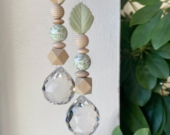Puede incluir: Dos adornos colgantes con esferas de cristal transparente facetado suspendidas de hilos de cuentas. Cada hebra incluye una cuenta en forma de hoja, cuentas redondas estriadas, cuentas redondas con patrones botánicos verdes y cuentas geométricas.