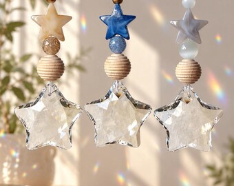 Puede incluir: Tres adornos colgantes con estrellas de cristal facetado transparente suspendidas de cordones blancos. Cada adorno incluye una cuenta de madera estriada, una cuenta redonda y una cuenta superior en forma de estrella beige, azul o gris.