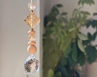 Puede incluir: Un adorno colgante con una lágrima de cristal facetado transparente en la base, seguida de una cuenta de madera estriada, dos cuentas de madera lisas, una cuenta estriada transparente, una pieza de vidrio cuadrada con una estrella y una cuenta pequeña.