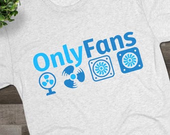 May include: A light gray t-shirt with the text "OnlyFans" in blue, accompanied by blue fan graphics. The shirt is displayed on a wooden surface, with black sneakers and eyeglasses visible.