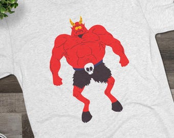 May include: A light gray heathered t-shirt featuring a graphic of a muscular red devil character with yellow horns, wearing dark shorts with a white skull belt buckle. The character has a goatee, wide eyes, and cloven hooves for feet.