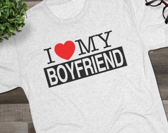 May include: A light gray heathered t-shirt featuring the black text I MY and a red heart symbol, with the word BOYFRIEND printed in white inside a black rectangular block. The shirt has short sleeves and a crew neckline, presented in a flat lay.