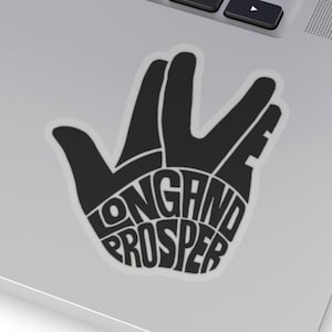May include: Black sticker in the shape of the Vulcan salute hand gesture. The words "Live Long and Prosper" are written inside the hand. The sticker is on a silver laptop.