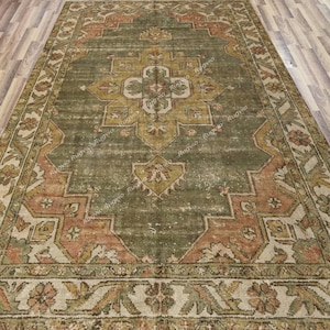 May include: An antique-style area rug with a distressed appearance. The rug features a central medallion design in shades of gold and olive green, framed by a border of peach and cream floral patterns. The rug is rectangular and appears to be made of woven material.