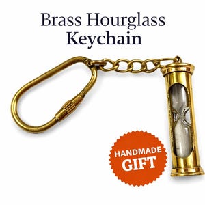 May include: A brass hourglass keychain with a clear glass centre. The keychain includes a gold-coloured clasp and chain. The text "Brass Hourglass Keychain" is at the top of the image, and a "Handmade Gift" sticker is at the bottom.