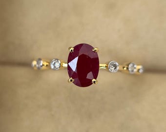 Könnte beinhalten: Ein goldener Ring mit einem ovalen, tiefroten Rubin als Mittelpunkt. Das Band ist mit kleinen, runden, klaren Edelsteinen verziert. Das Design des Rings ist schlicht, aber elegant und unterstreicht die leuchtende Farbe des Rubins.