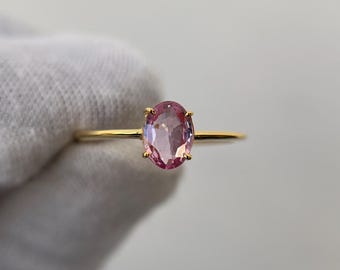 May include: A delicate gold ring featuring a light pink oval gemstone. The gemstone is the focal point, set on a thin, polished gold band. The ring is simple and elegant, suitable for everyday wear or special occasions.