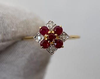 May include: A gold ring with a floral design, featuring oval-cut ruby gemstones at the centre and diamond accents. The ring has a thin, polished gold band. The gemstones are arranged in a cluster.
