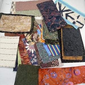 May include: A collection of assorted fabric scraps featuring various patterns and textures, including floral prints, geometric designs, stripes, solid colors, and abstract motifs in shades of orange, blue, green, brown, black, and white.