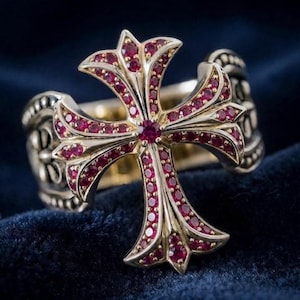 Puede incluir: Un anillo de oro con una cruz prominente en el centro adornada con numerosas piedras preciosas rojas, pequeñas y redondas. La banda del anillo muestra intrincados detalles metálicos en relieve a los lados, lo que le da una apariencia texturizada.