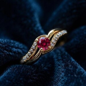 May include: A gold ring featuring a round, vibrant red gemstone at the centre, flanked by two curved bands encrusted with small, clear, sparkling stones. The design showcases a polished gold finish that highlights the deep red centre stone.