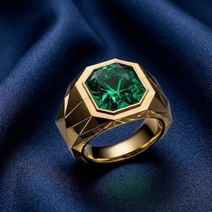 May include: A gold ring with a large, faceted emerald-green gemstone. The ring has a geometric design with a gold band and a square-cut emerald. The ring is set against a blue background.