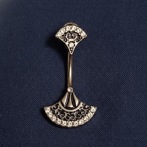 May include: Silver-toned belly button ring with a fan-shaped design. The top and bottom fan shapes are adorned with small, clear crystals. The ring has a curved, elongated stem connecting the two fan-shaped ends.