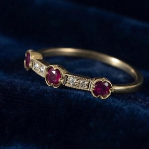 Könnte beinhalten: Ein Goldring mit drei rund geschliffenen roten Rubinen und zwei kleinen klaren Diamanten in einer Reihe. Die Metallfassung weist einen texturierten Rand im Milgrain-Stil um jeden Stein auf, was ein detailliertes, lineares Design auf dem Ring erzeugt.