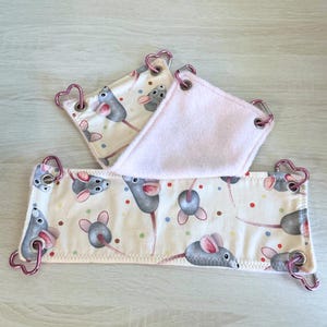 以下が含まれることがあります： 3つの小さなペット用ハンモック。ハンモックは、灰色のネズミとカラフルな水玉模様の繰り返し模様のクリーム色です。端はピンク色の生地とハート型の金属クリップでトリミングされています。