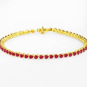 May include: A gold bracelet set with a line of vivid red gemstones. The gemstones are round and evenly spaced along the bracelet. The clasp is also gold-coloured. The bracelet is a classic piece of jewellery.
