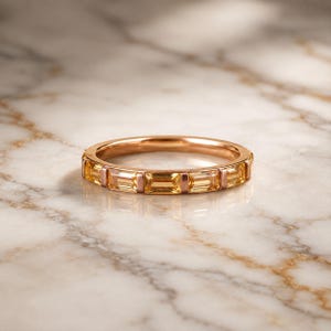 Könnte beinhalten: Ein Ring aus Roségold mit einer Reihe von rechteckigen, im Baguetteschliff geschliffenen gelben Citrin-Edelsteinen, die in einer Kanalfassung gesetzt sind. Das Metall hat ein warmes, poliertes Finish, das den goldenen Farbton ergänzt.
