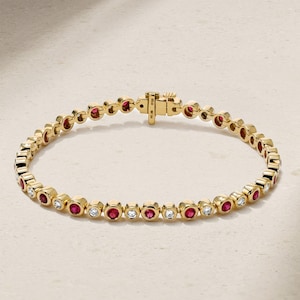 Könnte beinhalten: Ein goldenes Armband mit abwechselnd roten und klaren Edelsteinen. Das Armband hat einen sicheren Verschluss und wird auf einem neutralen Hintergrund präsentiert. Die Edelsteine sind in einzelnen Fassungen gefasst.