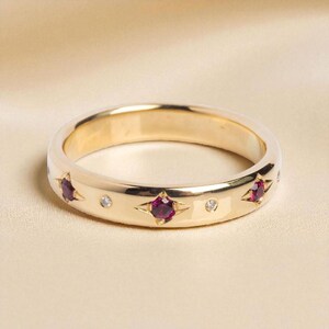 Könnte beinhalten: Ein goldener Ring mit abwechselnd sternförmigen Rubinen und kleinen Diamantakzenten. Der Ring hat eine glatte, polierte Oberfläche und ein klassisches Banddesign. Die Edelsteine sind bündig mit der Oberfläche des Bandes eingesetzt.