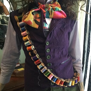 May include: A purple velvet vest with a colorful bow tie and a long chain of spools of thread around the waist.