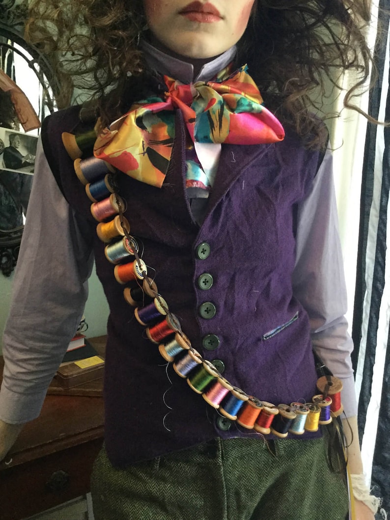 May include: A purple velvet vest with a colorful bow tie and a long chain of spools of thread around the waist.