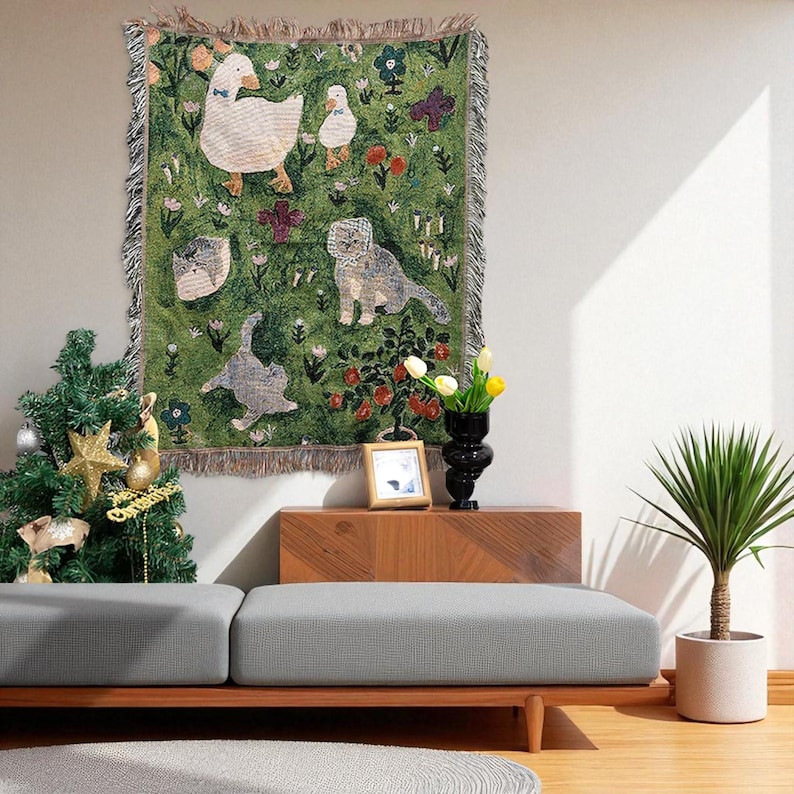 May include: A green tapestry with a whimsical design featuring geese, cats, flowers, and butterflies. The tapestry has a fringed border and is displayed on a wall. The color palette includes green, white, grey, and touches of red and purple.