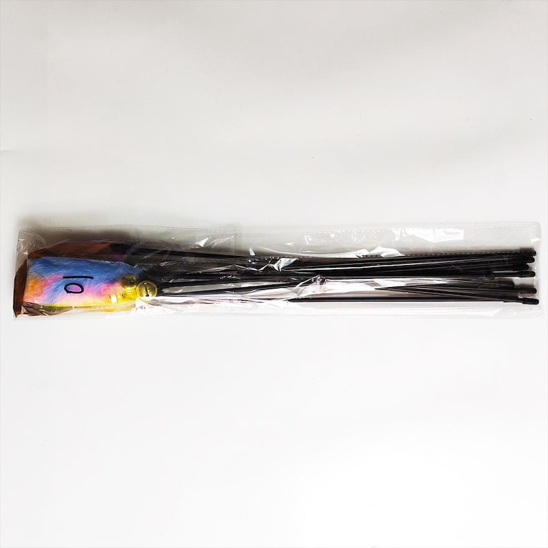 May include: A cat toy with a colorful, fluffy end and black rods. The fluffy end has blue, yellow, and pink hues, with the number "10" written on it. The toy is packaged in a clear plastic bag.