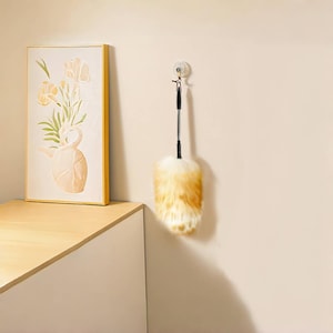 Peut inclure: Un plumeau avec un manche noir et une ventouse pour suspendre. Le plumeau est composé d'un mélange de plumes blanches et jaune-brun. Une peinture encadrée de fleurs dans un vase est sur une surface en bois.