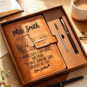 Peut inclure: Un carnet en similicuir beige dans un coffret cadeau avec un stylo assorti. La couverture présente une illustration de Winnie l'ourson, le nom Miss Smith et la citation : IT MAKES SUCH A DIFFERENCE, SAID POOH, TO HAVE SOMEONE WHO BELIEVES IN YOU. Love Sophia.