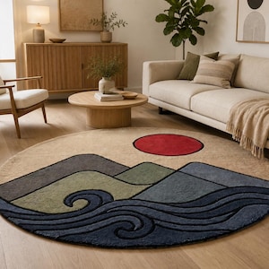 May include: A round area rug featuring a landscape design with a large red sun, layered mountains in shades of grey, sage green, and blue, and stylised dark blue ocean waves at the bottom, all set against a light beige background.
