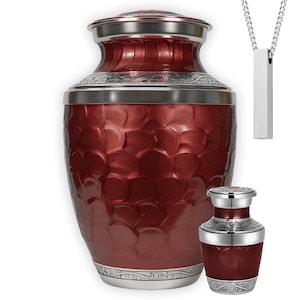 May include: A burgundy urn with a textured surface and silver accents. The urn has a matching miniature version and a silver pendant necklace. The urns are designed with a decorative pattern and a secure lid.
