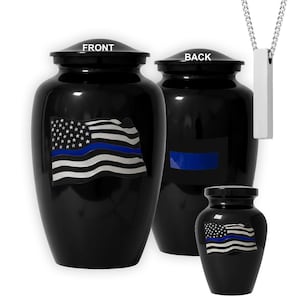 May include: Black urns with a blue line American flag design. The front of the urns are labeled "FRONT" and the back is labeled "BACK". A silver pendant with a rectangular shape hangs from a silver chain.