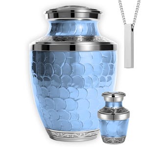 May include: A light blue urn with a textured pattern, silver accents, and a matching miniature urn. A silver pendant necklace with a rectangular bar is also included. The urns are designed with a decorative pattern.