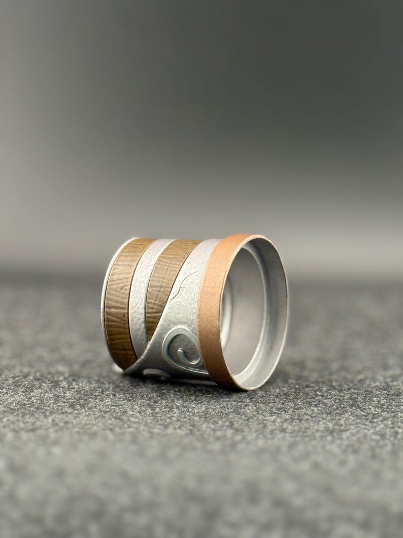 Puede incluir: Un anillo cil&iacute;ndrico con bandas alternas de veta de madera marr&oacute;n, plata y metal color cobre. La banda plateada presenta un dise&ntilde;o de remolino decorativo. El interior del anillo es de color plateado liso.