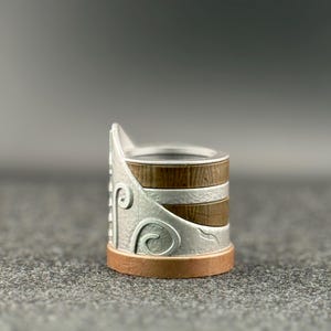 Puede incluir: Un portaanillos decorativo con un dise&ntilde;o de metal plateado y detalles en madera marr&oacute;n. La base es de color cobre. El portaanillos tiene un dise&ntilde;o &uacute;nico y en capas, perfecto para exhibir anillos.