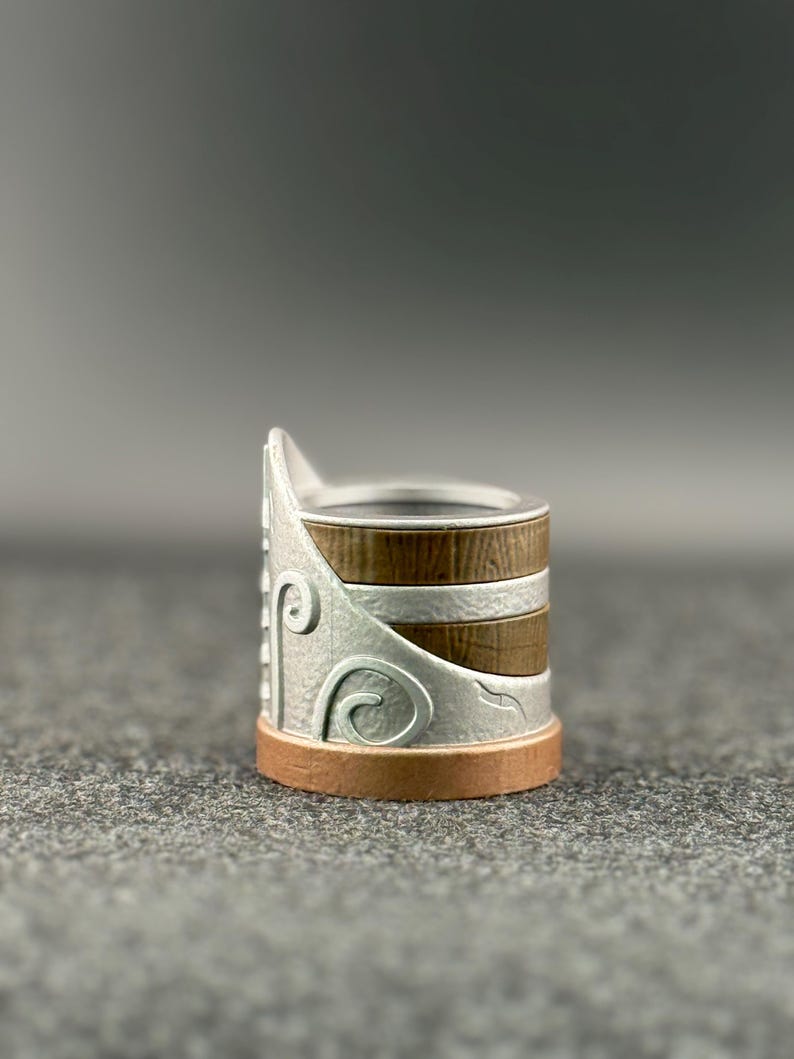 Puede incluir: Un portaanillos decorativo con un dise&ntilde;o de metal plateado y detalles en madera marr&oacute;n. La base es de color cobre. El portaanillos tiene un dise&ntilde;o &uacute;nico y en capas, perfecto para exhibir anillos.