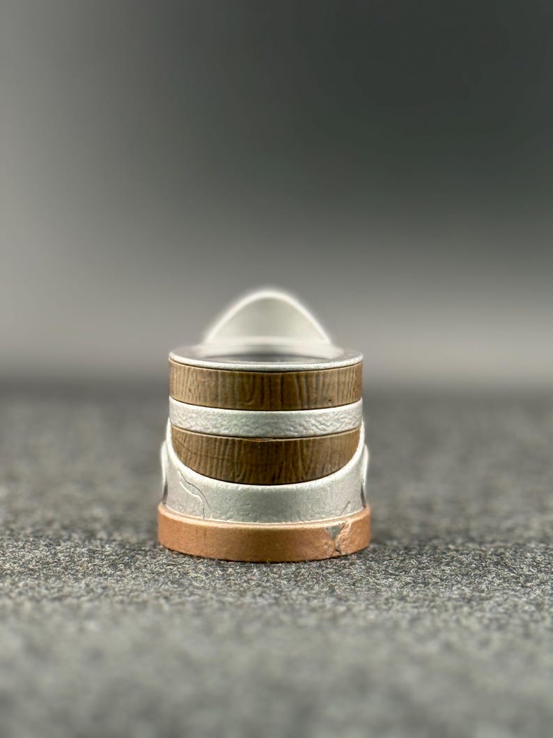 Puede incluir: Un peque&ntilde;o recipiente decorativo con tapa. El recipiente tiene forma cil&iacute;ndrica con bandas alternas de metal marr&oacute;n, plateado y color cobre. La tapa es plateada y tiene un asa arqueada y curvada.