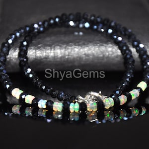 May include: A black beaded necklace with a silver clasp. The necklace features small, faceted black beads interspersed with iridescent opal beads. The text "ShyaGems" is visible on the image.