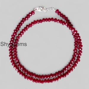May include: A layered necklace with faceted, deep red gemstones. The necklace has a silver-coloured clasp. The text "Shyagems" is visible. The gemstones are arranged in multiple strands. The necklace is a vibrant accessory.