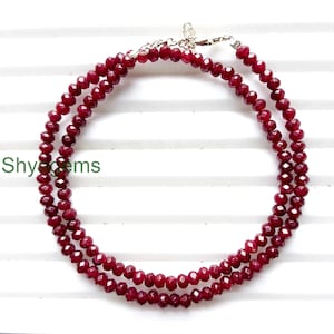 May include: A layered necklace featuring faceted, deep red gemstones. The necklace is composed of multiple strands of small, round beads, creating a rich, textured appearance. The clasp is silver-toned. The text "Shygems" is visible in the image.