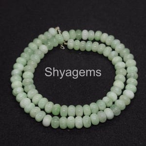 May include: A necklace composed of light green, rounded beads. The beads are strung together with a silver clasp. The text "Shyagems" is displayed in white letters across the center of the necklace, against a black background.
