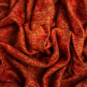 Puede incluir: Primer plano de una tela tejida roja y naranja con una superficie texturizada. La tela est&aacute; doblada y drapeada, creando un aspecto suave y acogedor.