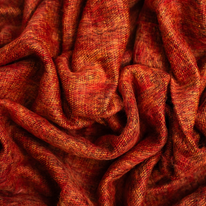 Puede incluir: Primer plano de una tela tejida roja y naranja con una superficie texturizada. La tela est&aacute; doblada y drapeada, creando un aspecto suave y acogedor.