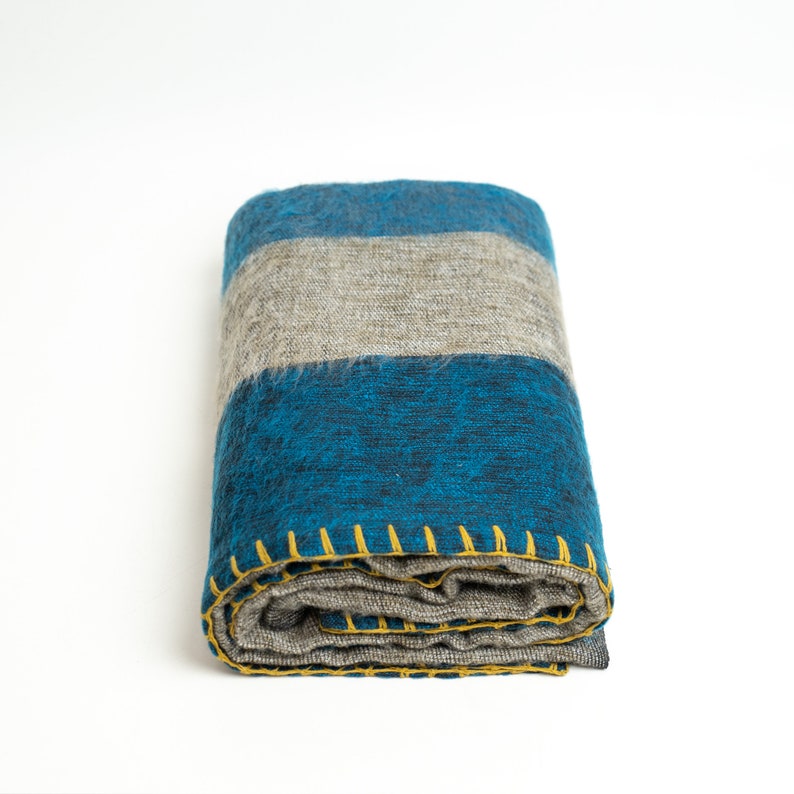 May include: A folded blue and gray striped throw blanket with yellow stitching around the edges.