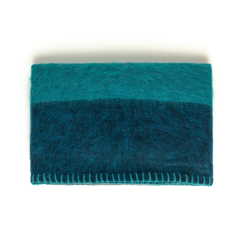 May include: A teal and dark blue throw blanket with a stitched edge.