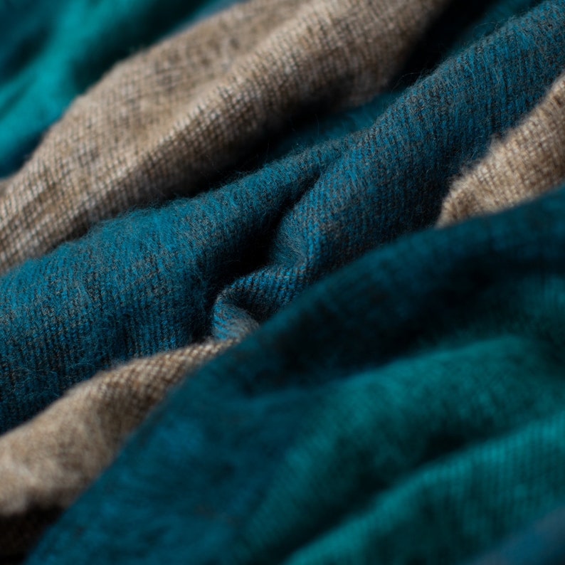 May include: Close-up of a soft, textured fabric with a blue and beige color scheme. The fabric is folded and draped, creating a sense of warmth and comfort.